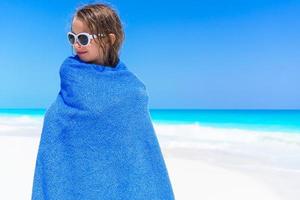 adorável menina enrolada em toalha na praia tropical depois de nadar no mar foto