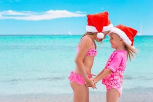 meninas adoráveis em chapéus de Papai Noel durante as férias na praia se divertem juntos foto