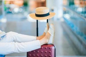 jovem mulher em um saguão do aeroporto esperando o pouso. pernas de closeup na bagagem foto
