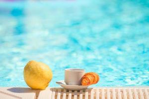 delicioso café da manhã limão, café, croissant à beira da piscina foto