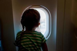 menina olhando pela janela do avião. adorável criança viajando de avião foto