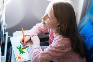 adorável menina viajando de avião. garoto desenhando com lápis coloridos sentado perto da janela da aeronave foto