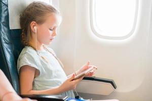 adorável menina viajando de avião. garoto bonito com laptop perto da janela em aeronaves foto