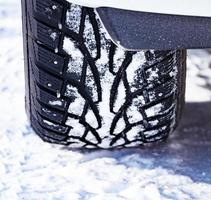 tiro de close-up de pneu cravejado de automóvel coberto de neve na estrada de neve de inverno foto