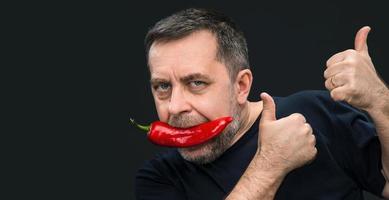 homem idoso com pimenta vermelha na boca foto