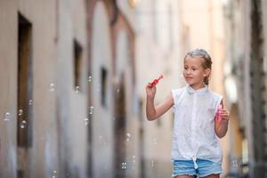 adorável menina ao ar livre soprando bolhas de sabão na cidade europeia. retrato de criança caucasiana aproveita as férias de verão na Itália foto