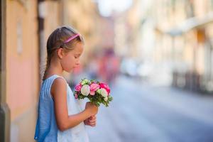 menina adorável com buquê de flores andando na cidade europeia foto