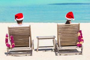 jovem casal de chapéu de papai noel relaxando na praia tropical durante as férias de natal foto