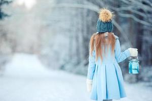 menina adorável com lanterna no natal na floresta de inverno ao ar livre foto