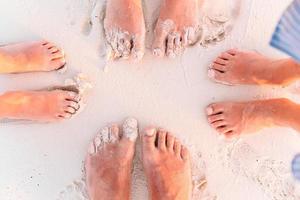 close-up dos pés da família na praia de areia branca foto