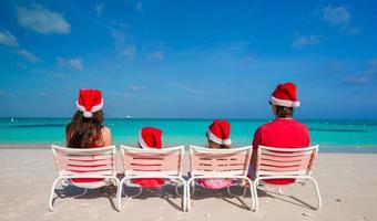 família de quatro pessoas feliz em chapéus de natal na praia branca foto