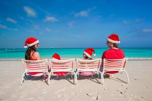 família de quatro pessoas feliz em chapéus de natal na praia branca foto