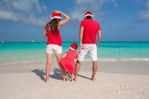 família feliz de três em chapéus de natal durante as férias tropicais foto