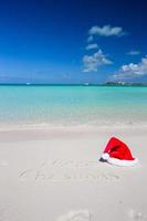 feliz natal escrito na areia branca da praia tropical com chapéu de natal foto