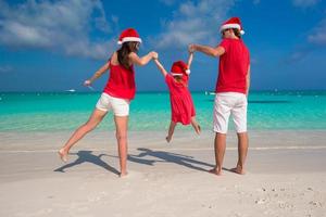 família feliz de três em chapéus de natal durante as férias tropicais foto