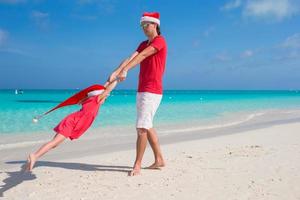 menina e pai feliz com chapéu de Papai Noel se divertem na praia tropical foto