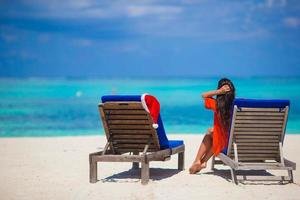 chapéu de papai noel vermelho na cadeira longue na praia branca tropical foto