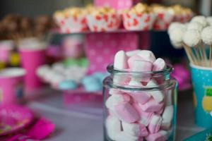 marshmallow, merengues de cores doces, pipoca, bolos de nata e cake pops na mesa foto