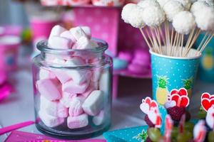 marshmallow, merengues de cores doces, pipoca, bolos de nata e cake pops na mesa foto