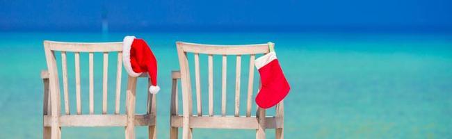 meia vermelha de natal e chapéu de papai noel na cadeira na praia tropical branca foto