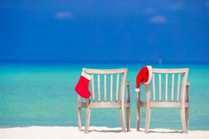 meia vermelha de natal e chapéu de papai noel na cadeira na praia tropical branca foto