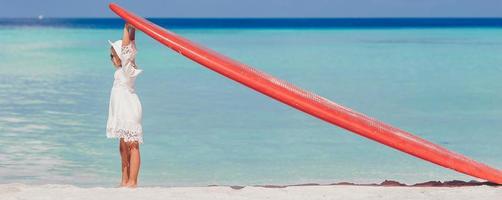 menina adorável com prancha de surf grande vermelha na praia branca tropical foto