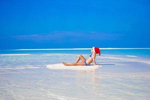 adorável menina de chapéu de Papai Noel na praia durante as férias foto