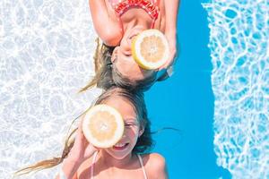 meninas cobrindo os olhos com metades de limão perto dos olhos na piscina de fundo foto