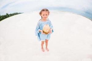 menina adorável com grande coco na praia de areia branca foto