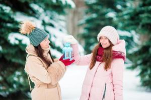 meninas segurando a luz de velas de natal ao ar livre no lindo dia de neve de inverno e aquecem as mãos foto