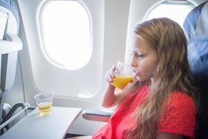 adorável menina viajando de avião. garoto bebendo suco de laranja sentado perto da janela do avião foto