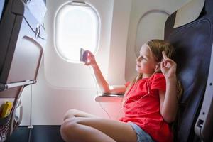 adorável menina viajando de avião. garoto sentado perto da janela do avião foto