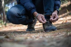 jovem caminhante amarra os cadarços de seu sapato enquanto mochila na floresta foto