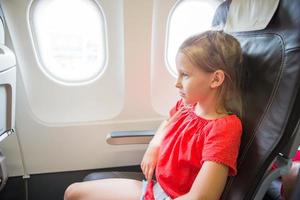 adorável menina viajando de avião. garoto sentado perto da janela do avião foto