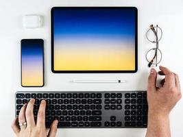 vista superior das mãos em um teclado com um tablet e telefone foto