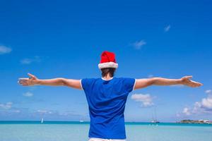 vista traseira do jovem com chapéu de Papai Noel na praia tropical foto