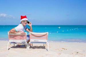 vista traseira do jovem com chapéu de natal na cadeira de praia foto