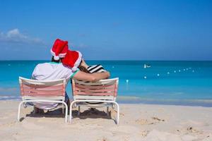 vista traseira do casal em chapéus de papai noel aproveite as férias na praia foto