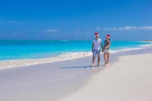 jovem casal feliz em chapéus de papai noel vermelhos na praia de areia tropical foto