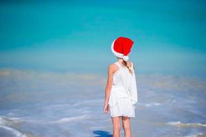 adorável menina com chapéu de Papai Noel em praia tropical foto