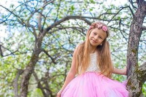 menina adorável sentada na árvore florescendo no jardim de maçã foto