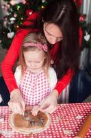 menina com jovem mãe fazendo biscoitos de gengibre de natal juntos foto