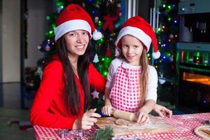 família feliz em chapéus de papai noel assando biscoitos de gengibre de natal juntos foto