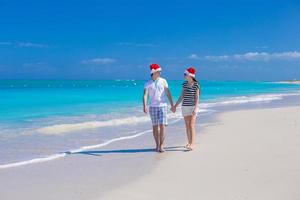 jovem casal feliz em chapéus de papai noel vermelhos na praia tropical foto