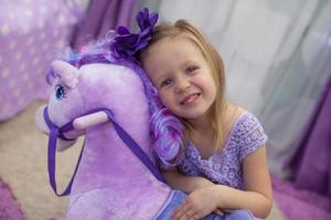 menina bonitinha feliz brincando com um cavalo de brinquedo em casa foto