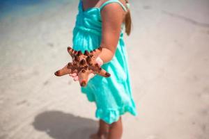 menina adorável com estrela do mar nas mãos na praia tropical foto