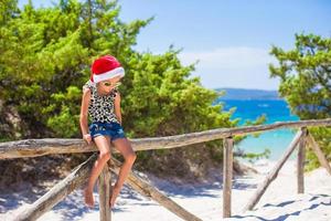 menina bonitinha com chapéu de natal durante as férias na praia foto
