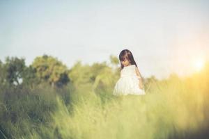 menina feliz em pé na campina em um vestido branco foto