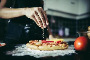 close-up de uma mão colocando orégano sobre uma pizza foto