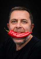 homem idoso com pimenta vermelha na boca foto